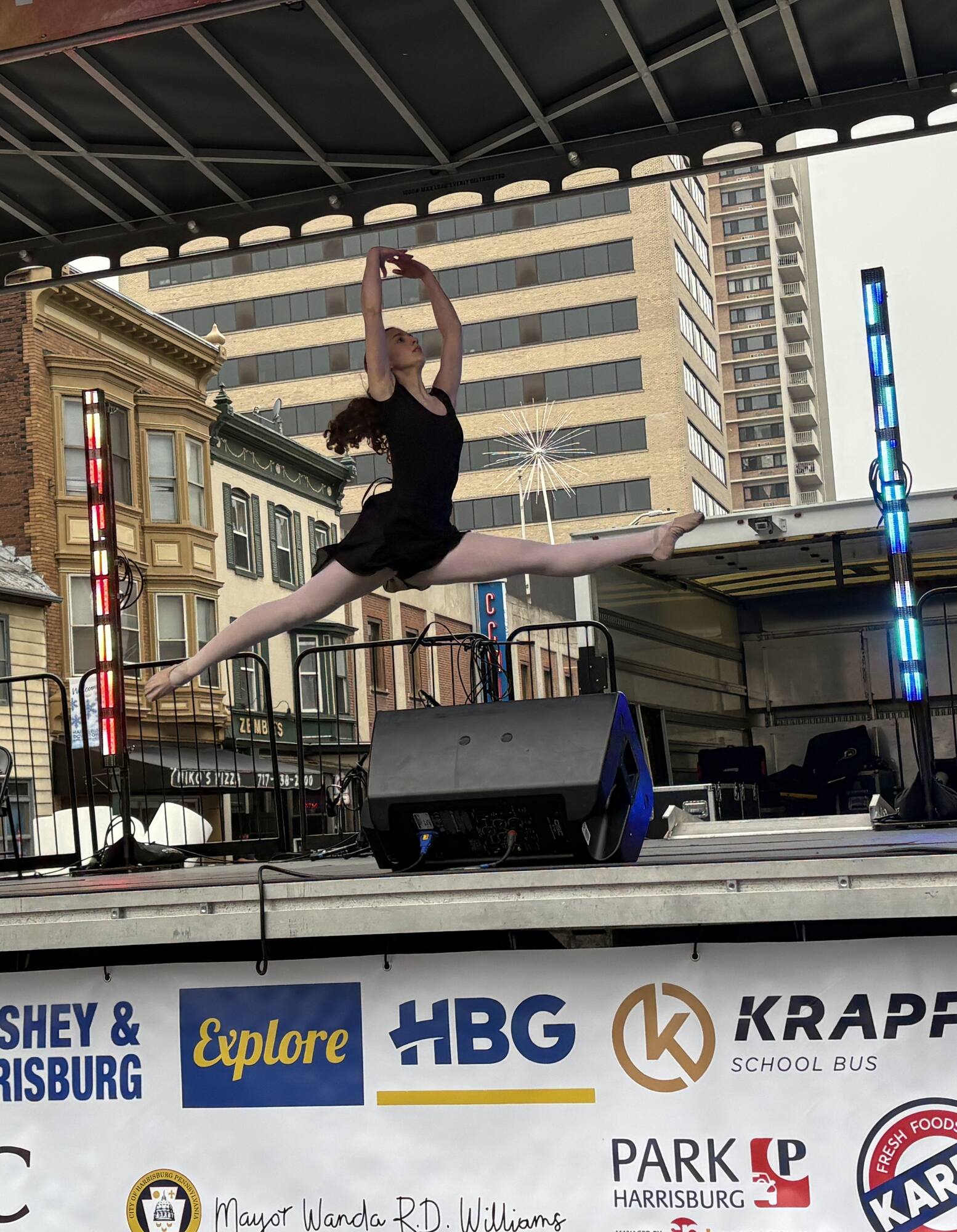 A dancer leaps in a full split on an outdoor community stage