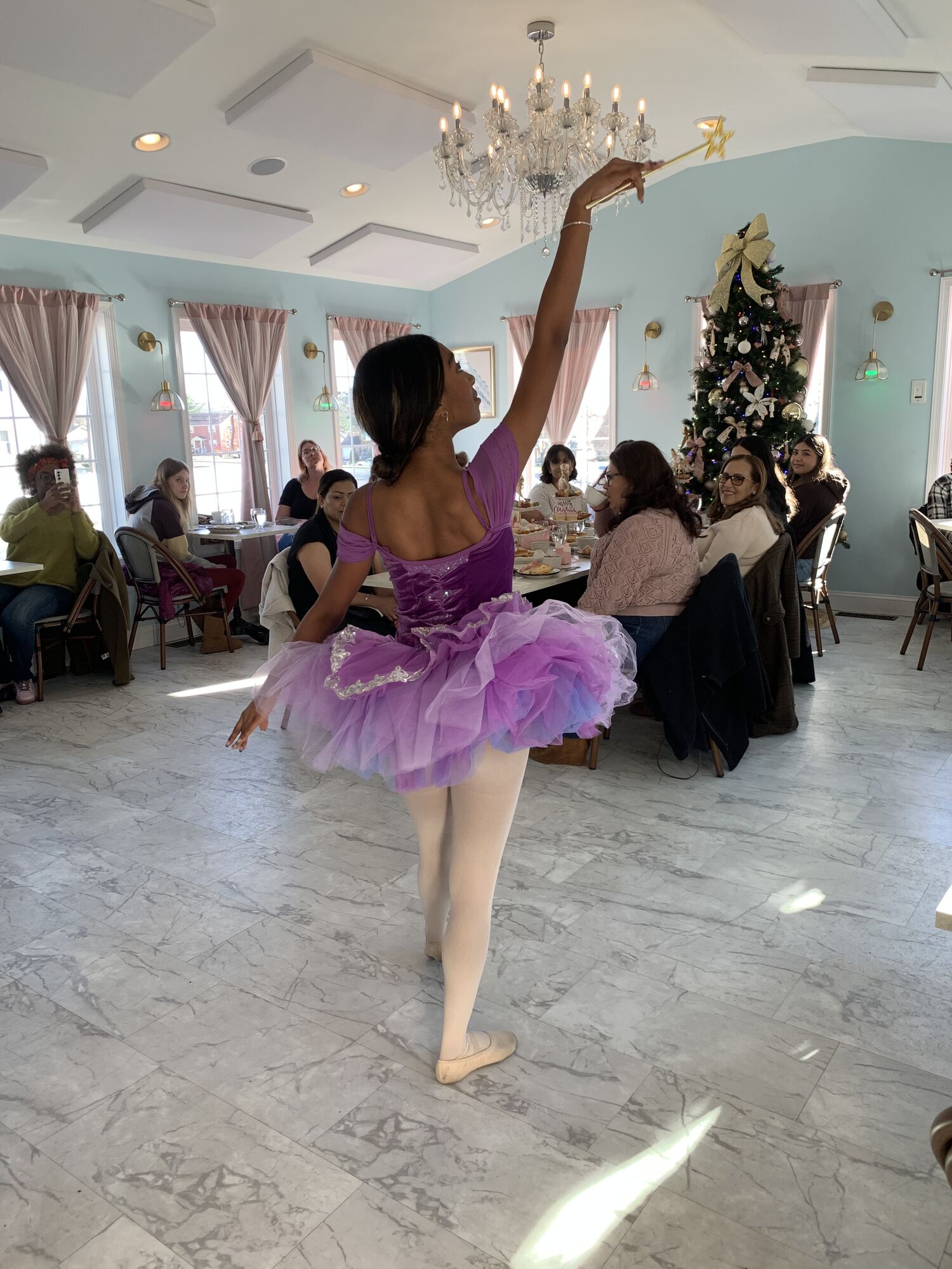 A Nutcracker dancer in a lilac tutu poses in arabesque at a community tea party
