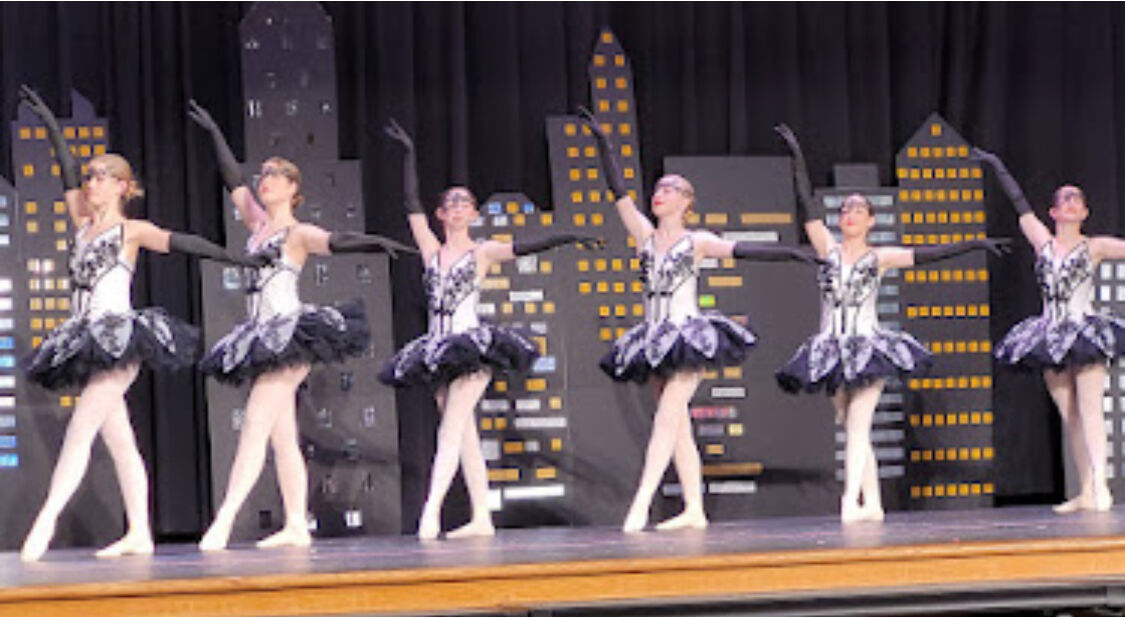 Six ballerinas in black-and-white tutus posing in a unison line