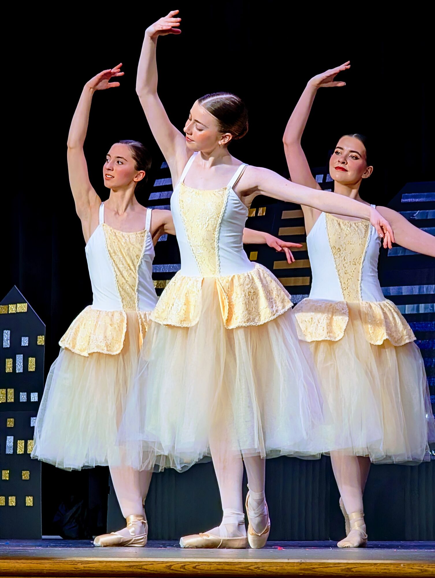 Three ballerinas en pointe in cream tutus with arms raised