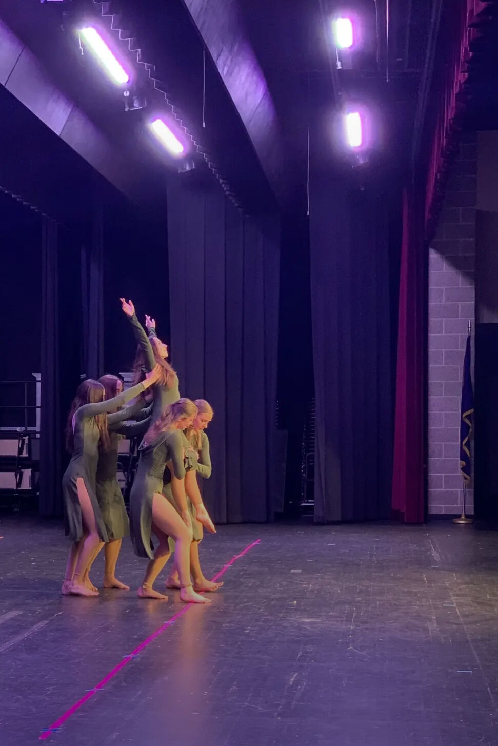 Lyrical dancers lift a teammate skyward under purple stage lights