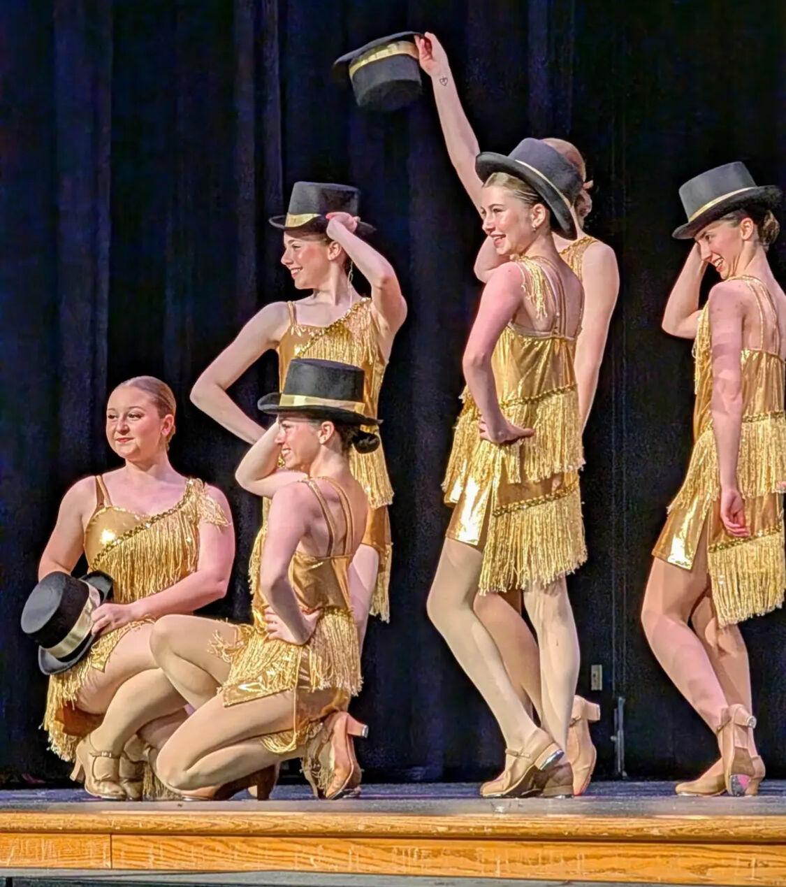 Tap dancers in gold fringe costumes tipping top hats on stage